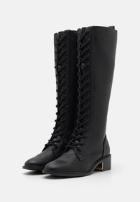 Knähöga svarta läderstövlar med spetsig tå, utrustade med en full lace-up fram och en låg staplad klack med en guldig accentdetalj.