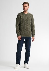 Sweter w splot kablowym w oliwkowym kolorze, z okrągłym dekoltem i ściągaczami przy mankietach. W zestawieniu z ciemnoniebieskimi chinosami i białymi sneakersami.