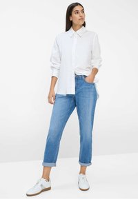 Witte overhemd met lange mouwen, gecombineerd met lichtblauwe opgerolde jeans en witte sneakers met een bruine zool.