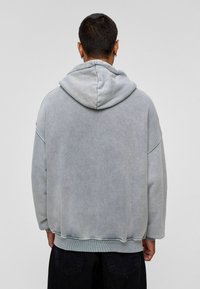 Grijze oversized hoodie met een gestructureerde afwerking, voorzien van een grote capuchon en rib gebreide zoom. De stof lijkt zacht en versleten met zichtbare stikseldetails.