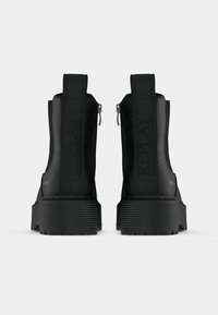 Para czarnych, masywnych botków na platformie sięgających kostek, z tylnym zamkiem błyskawicznym i markowymi uchwytami, widziana od tyłu na białym tle.