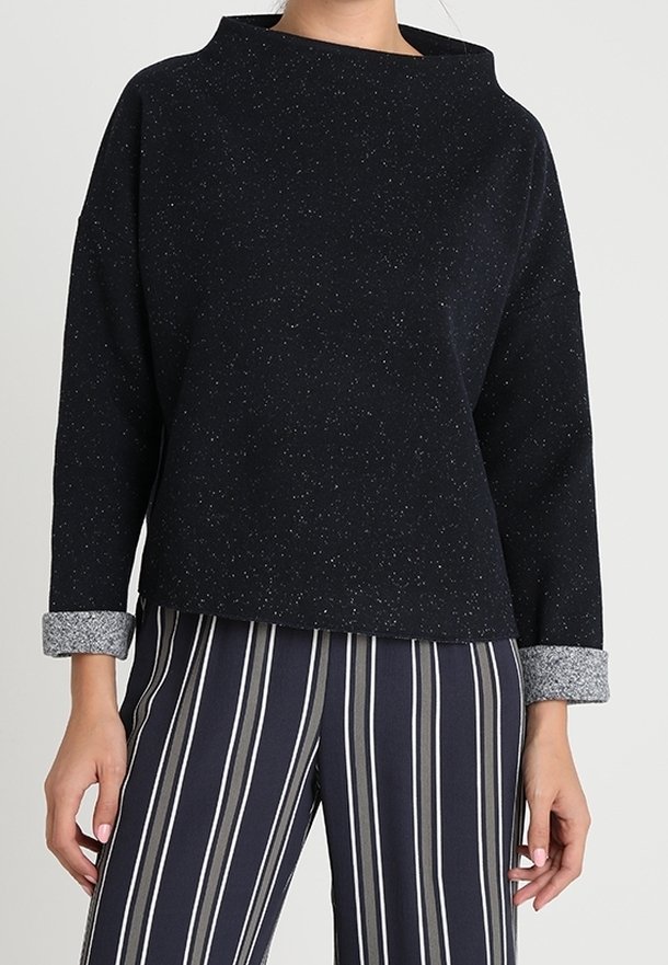 Svart, prickig tröja med en bred, rundad halsringning och långa ärmar, med grå, manschettaccentuerade detaljer. Matchas med randiga, högmidjade byxor.