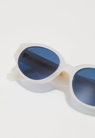 White, rounded sunglasses with blue lenses, featuring a thick frame and visible branding on the lens. Smooth texture, modern design.