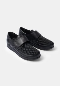 Chaussures noires avec un avant en tissu tissé texturé et une bride en cuir lisse. Bout arrondi et semelle rembourrée pour plus de confort.