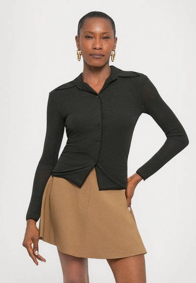 Camicia nera a maniche lunghe con abbottonatura frontale e vestibilità slim, abbinata a una gonna a trapezio color beige. Tessuto liscio con design su misura.