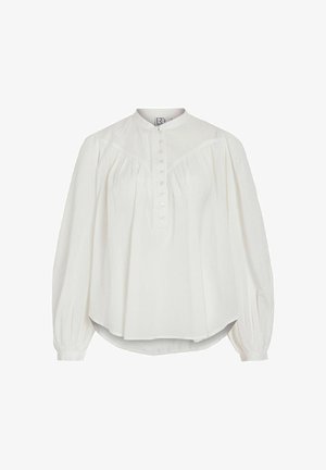 Vit blus med lång ärm, hög krage och knäppning framtill. Har rynkad tygdetalj vid axlarna och rundad nederkant. Tillverkad av lätt material.