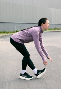 Sportlik riietus, mis sisaldab heledat lillat pikkade varrukatega särki, musti retuuse tekstuursete detailidega ja musti jooksutossusid valge tallaga.