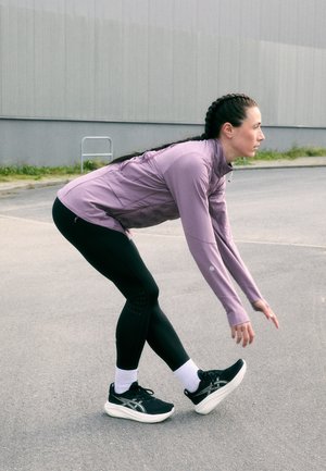 Träningskläder som består av en ljuslila långärmad topp, svarta leggings med texturerade detaljer och svarta löparskor med vita sulor.