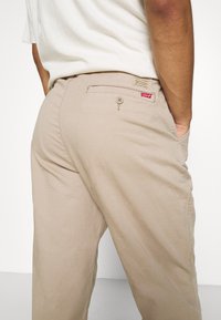 Beige chinos made of cotton with a straight-leg cut, featuring a buttoned back pocket and a red Levi's logo tag.