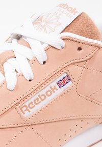 Ljust rosa mocka Reebok-sneakers med vita snören, en vadderad tunga och en logotags som visar den brittiska flaggan. Solid gummisula.