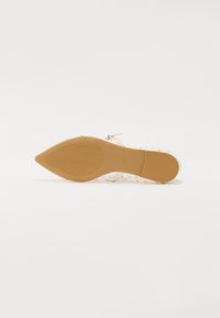 Chaussure à talon haut à bout pointu avec une tige translucide, blanche avec des pois dorés, et une semelle en caoutchouc beige dotée d'une texture antidérapante.
