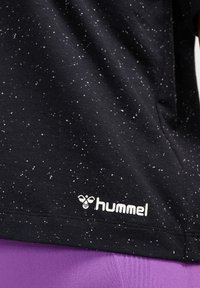 Svart T-shirt med ett prickigt mönster i vitt. Har "hummel"-logotypen i vitt. Materialet verkar mjukt och stretchigt.
