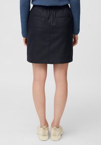 Mini jupe noire avec une taille élastique, deux poches arrière et une texture lisse. Assortie avec des chaussures de couleur claire.
