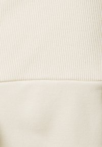 Světle zbarvená tkanina s jemným vroubkovaným vzorem nahoře a hladkým povrchem dole. Navrženo s kontrastními vzory v krémových odstínech.