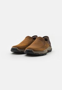 Pantofi din piele maro, tip slip-on, cu un design curbat, guler căptușit și talpă din cauciuc texturat. Accente notabile în negru și portocaliu pe talpă.