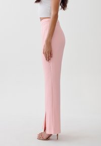 Lichtroze op maat gemaakte broek met een aansluitende hoge taille, zijsplitten en een gladde textuur, gecombineerd met lichtgekleurde strappy hakken.