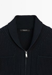 Pull noir en maille zippé avec col châle côtelé et étiquette visible indiquant Massimo Dutti fabriqué en Chine.