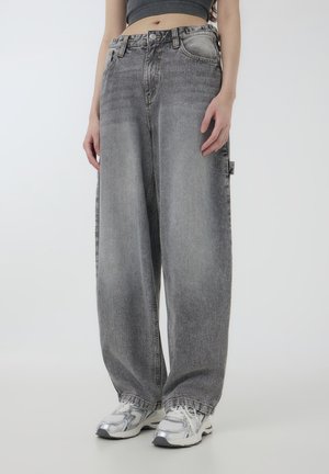 Jeans di denim grigio chiaro a gamba larga, con una finitura sbiadita e cuciture a contrasto. Abbinati a sneakers argento.