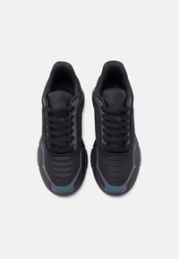 Par crnih atletski tenisica s debelim potplatima, mrežastom tkaninom i iridizirajućim detaljima na prstima, prikazan iz ptičje perspektive na bijeloj pozadini.