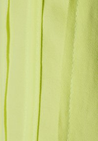 Nahaufnahme von hellgrünem Stoff mit vertikalen genähten Falten, die subtile Falten und Texturen erzeugen.