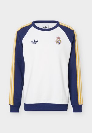 Biely crewneck mikina s námornícky modrými rukávmi, žltými pruhmi, logom Adidas na ľavej strane hrude a erbom Realu Madrid na pravej strane hrude.