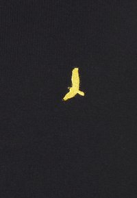 Black fabric with a textured weave featuring a small yellow bird logo embroidered on the front.