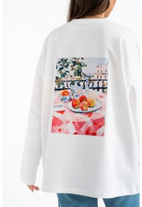 Felpa bianca oversize con una vivace stampa di mele e stoviglie su un tovagliolo a scacchi rosa sul retro.