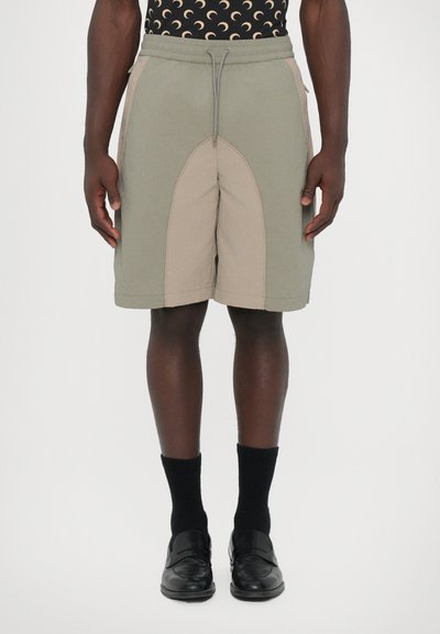 These shorts feature a two-tone design with a light beige and green color scheme, made from lightweight fabric, with an elastic waistband and drawstring.