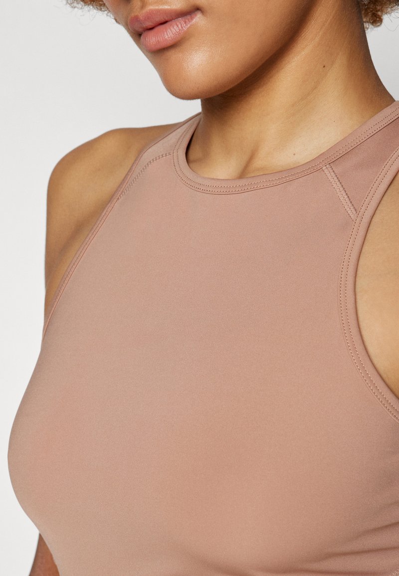 Top sportivo rosa chiaro, tessuto morbido, design aderente, spalline sottili, scollatura raccolta, cuciture dettagliate lungo i bordi.