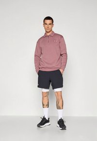 Heleroosa pika varrukaga polo särk lukuga kraega, kombineeritud tumeroheliste lühikeste pükstega. Modell kannab musti tenniseid ja valgeid sokke ning näitab jalgadel tätoveeringuid.