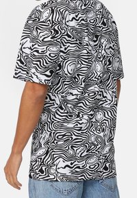 Krátký rukáv košile s černobílým vírovým vzorem s usmívajícími se tvářemi, z bavlněné látky, volnější střih a kulatý výstřih.