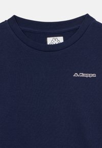 Tumši zils Kappa T-kreklis ar apaļu kaklu, kam priekšā augšējā kreisajā krūšu daļā ir neliels balts Kappa logo.