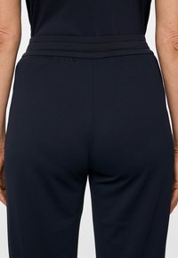 Granatowe spodnie sportowe z teksturowanym wykończeniem i szerokim elastycznym pasem, ozdobione dwoma poziomymi paskami.