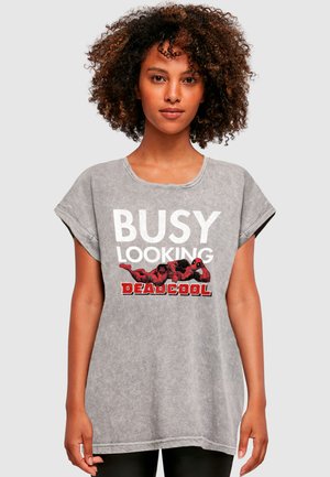 Grå oversized t-shirt med hvid og rød grafisk tekst, der står "BUSY LOOKING DEADCOOL", samt tegneseriefigurer. Blød tekstur, korte ærmer.