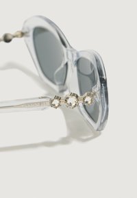 Przeciwsłoneczne, przezroczyste okulary w rozmiarze oversized w szarym kolorze z szarymi soczewkami, z ramieniem zdobionym kryształami i wygrawerowanym logo "Swarovski".