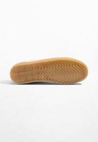 Tennaripohja, jossa kalanruotokuvio ja vaaleanruskeaa kumia, sileä beige yläreuna ja hillitty brändäys.