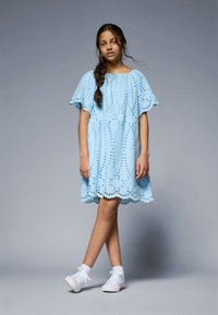 Lyseblå kort kjole med broderi, bølget nederkant og løse fladderermmer, kombinert med hvite sneakers.