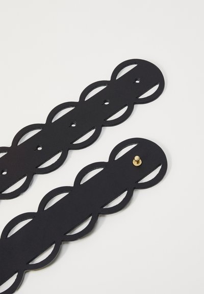 Black leather strap with cutout oval design and circular ends. Gold hardware stud detail for fastening. Smooth texture.