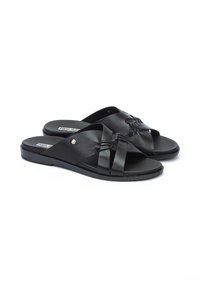 Chanclas negras con un diseño de tira trenzada ancha. Hechas de cuero suave, con suela plana y un remache dorado como acento.