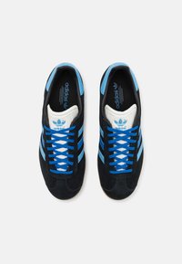 Μαύρα σουέντ αθλητικά παπούτσια με μπλε δερμάτινες ρίγες, λευκές λεπτομέρειες και μπλε κορδόνια. Διαθέτουν επενδεδυμένη γλώσσα και ελαστική σόλα.