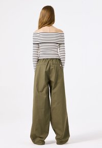 Gestreiftes, schulterfreies Oberteil in Schwarz und Weiß kombiniert mit lockeren, hoch taillierten olivgrünen Hosen, die einen elastischen Bund und seitliche Taschen haben.