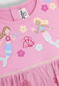 Robe en coton rose ornée de sirènes, de fleurs et de coquillages brodés. La jupe est superposée avec un détail en tulle brillant à l'ourlet.