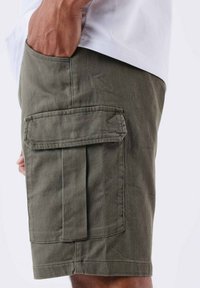 Pantalones cortos de cargo verde oliva hechos de una tela texturada, con un gran bolsillo lateral y un ajuste cómodo. Costuras visibles que acentúan el diseño.
