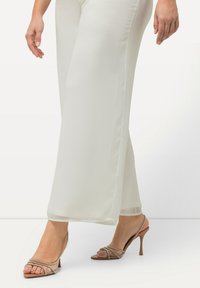 Lichtbeige wijde broek gemaakt van zachte stof, gecombineerd met naakte hoge hakken met straps en een spitse neus.