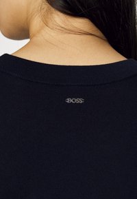 Pull bleu marine avec une texture côtelée, orné d'un logo argenté "BOSS" au dos, près de l'encolure.