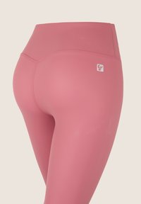 Leggings a vita alta rosa con una texture liscia, dotati di un sottile logo sul retro e cuciture piatte per comfort e supporto.