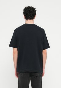 Μαύρο βαμβακερό T-shirt με λαιμόκοψη τύπου crew και κοντά μανίκια, με χαλαρή εφαρμογή και λεία υφή, φαίνεται από πίσω.