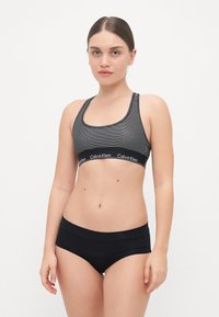 Svartstripete sportsbh med bredt bånd som har Calvin Klein-logoen, i kombinasjon med svarte boyshorts. Glatt stoff, minimalistisk design.