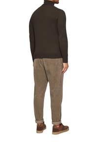 Un pull à col roulé vert foncé et un pantalon en velours côtelé marron clair. La tenue présente une coupe décontractée et des baskets brunes avec des accents texturés.