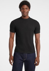 Czarny prążkowany t-shirt z krótkim rękawem, okrągłym dekoltem, dopasowany kształt i gładka tekstura, w połączeniu z ciemnymi dżinsami.